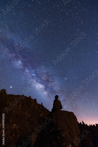 Young man looking at the stars and the milky way on a summer night in the mountains