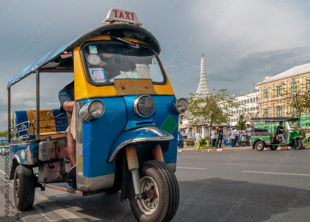 A typical tuk tuk taxi in the historic center of Bangkok, Thailand, with one of the most famous temples in the background