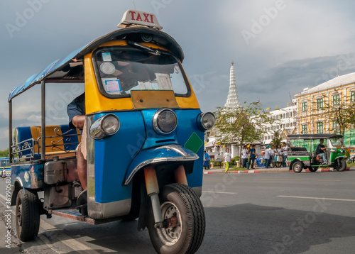 A typical tuk tuk taxi in the historic center of Bangkok, Thailand, with one of the most famous temples in the background