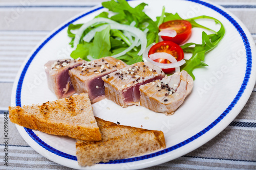 Picture of tasty lightly fried tuna, served at plate with bread and greens