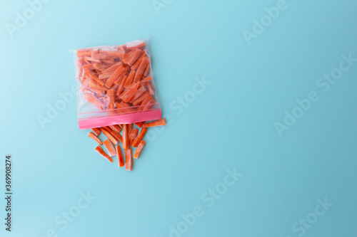 Plastic bag with frozen carrots on blue background, top view. Vegetable preservation