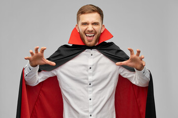 holiday, theme party and people concept - man in halloween costume of vampire and dracula cape scaring over grey background