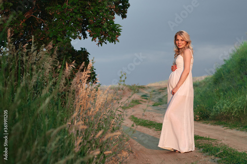 Pregnant young woman in white dress on posing in summer natural park