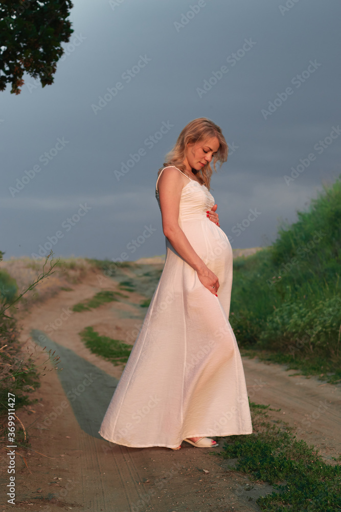 Pregnant young woman in white dress on posing in summer natural park