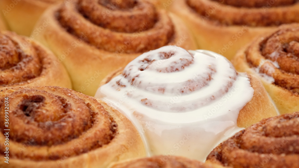 pouring fluffy frosting on Freshly baked cinnamon rolls or Cinnabon close up. Sweet cream cheese frosting pouring on cinnamon rolls