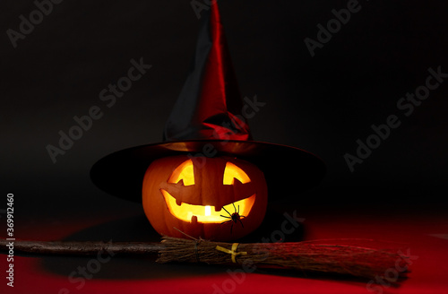 halloween and holiday decorations concept - jack-o-lantern in witch's hat with spider and broom in darkness
