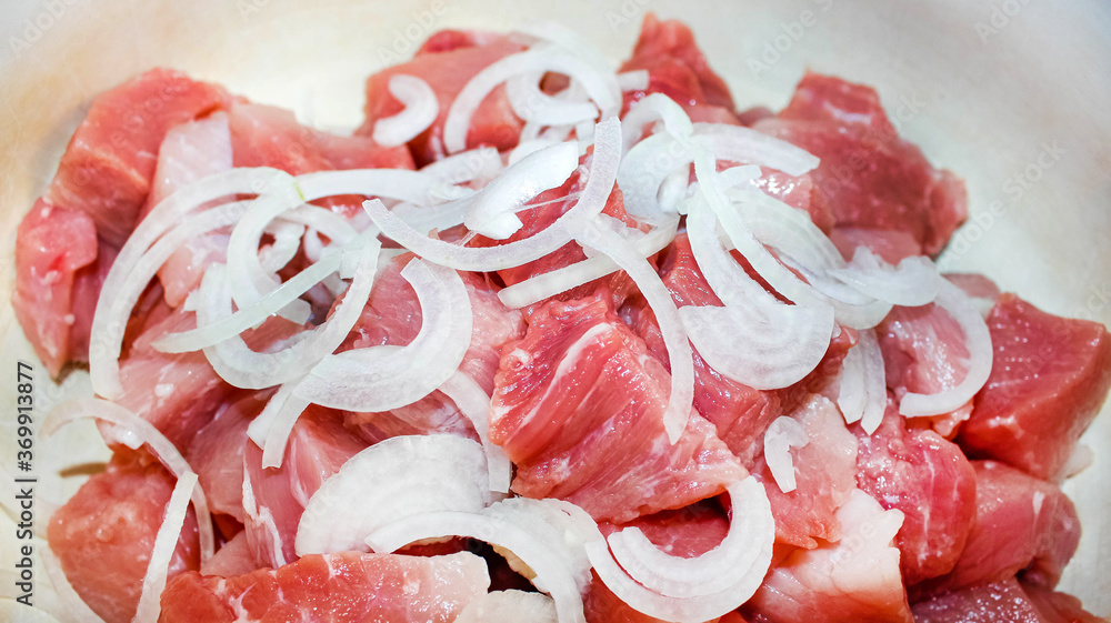 Raw meat cut into chunks with onion half-rings. Harvesting meat for a picnic.