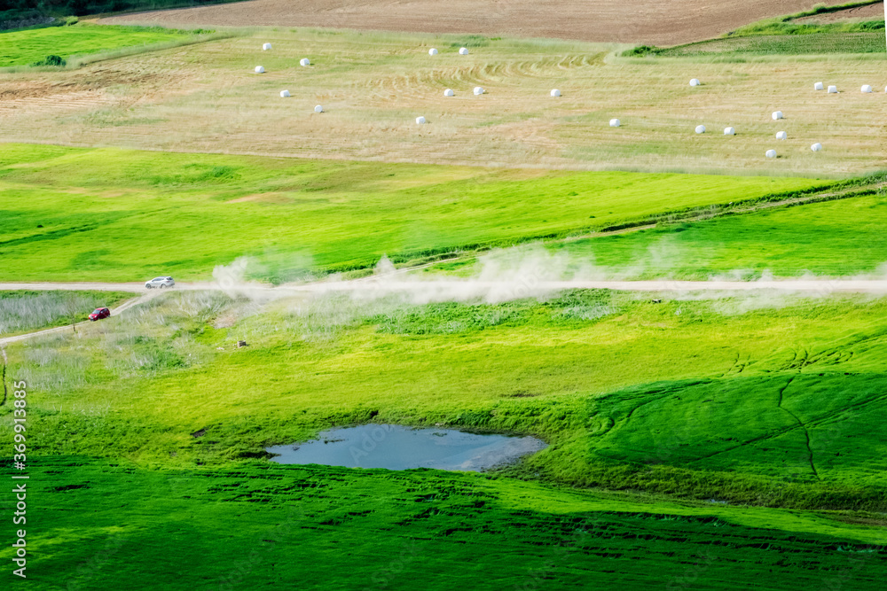 Vehicle driving on unpaved road making dust through the wonderful and beautiful rural scenic landscape,Avena Sativa,Oat green field. Vehicle driving on unpaved road making dust through the wonderful and beautiful rural scenic landscape,Avena Sativa,Oat green field.