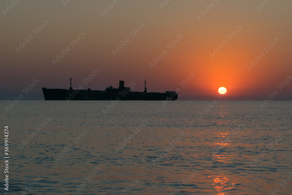Beautiful sunrise at sea. The silhouette of an abandoned wreck in the sea. Shipwrecked