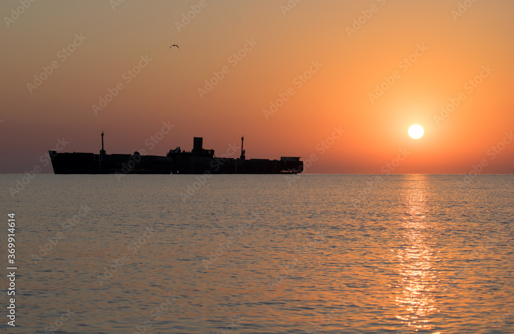 Beautiful sunrise at sea. The silhouette of an abandoned wreck in the sea