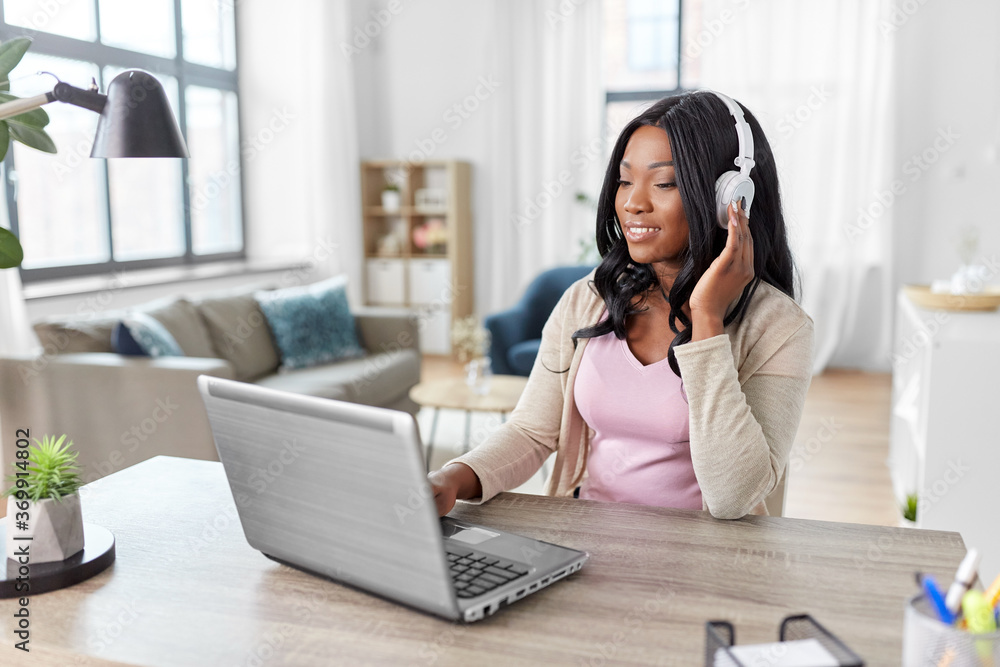 remote job, technology and people concept - happy smiling african american young woman in headphones with laptop computer working at home office remote job, technology and people concept - happy smiling african american young woman in headphones with laptop computer working at home office
