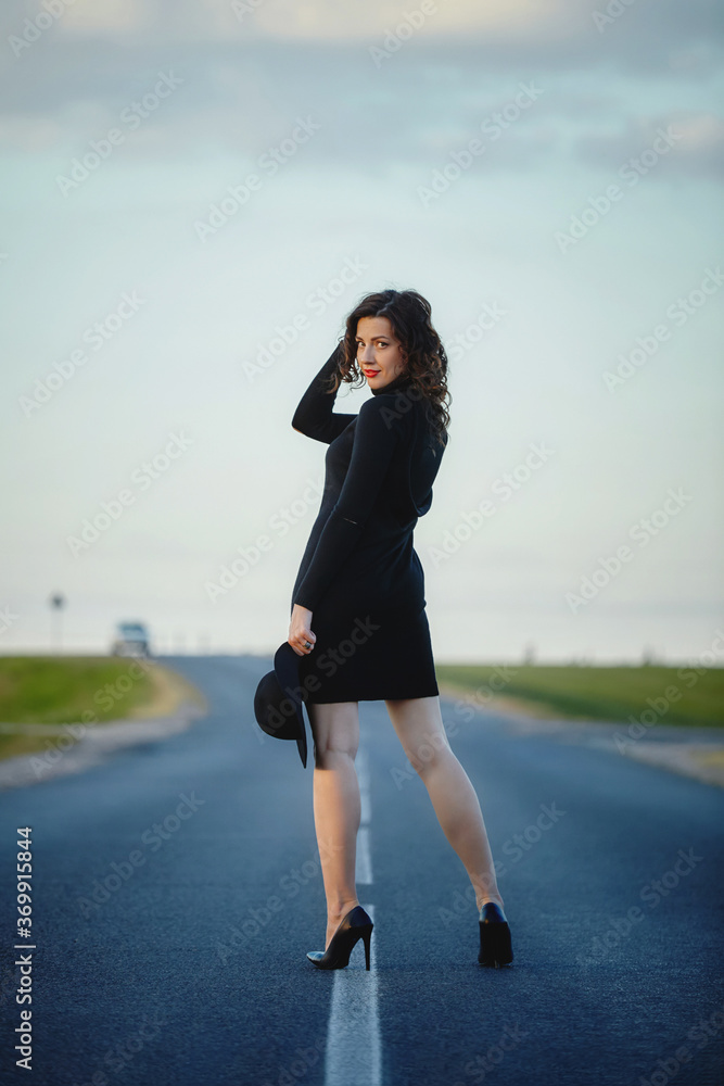 attractive girl in black dress and hat posing on the road with a dividing strip