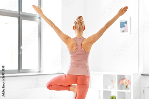 Fototapeta Naklejka Na Ścianę i Meble -  fitness, people and healthy lifestyle concept - young woman doing yoga in tree pose at home