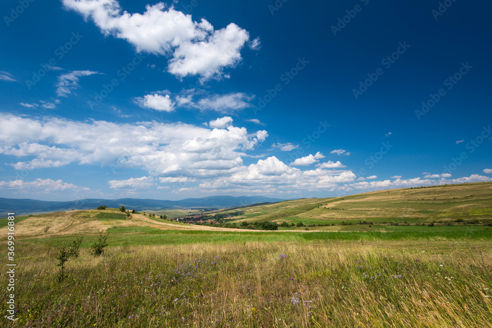 View from the top of a hill, small hungarian village in the valley in Transylvania, Romania, blue sky with white clouds background.