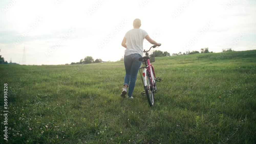Cinematic shot of a young woman walking on a green field with a bicycle on sunset time. Cinematic shot of a young woman walking on a green field with a bicycle on sunset time.