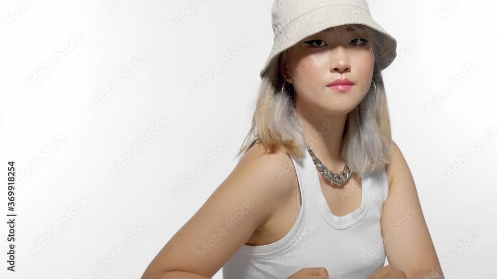 blonde Korean model portrait in studio with hair blowing wearing a 90s bucket hat and touches her hair and watching from side to side blonde Korean model portrait in studio with hair blowing wearing a 90s bucket hat and touches her hair and watching from side to side