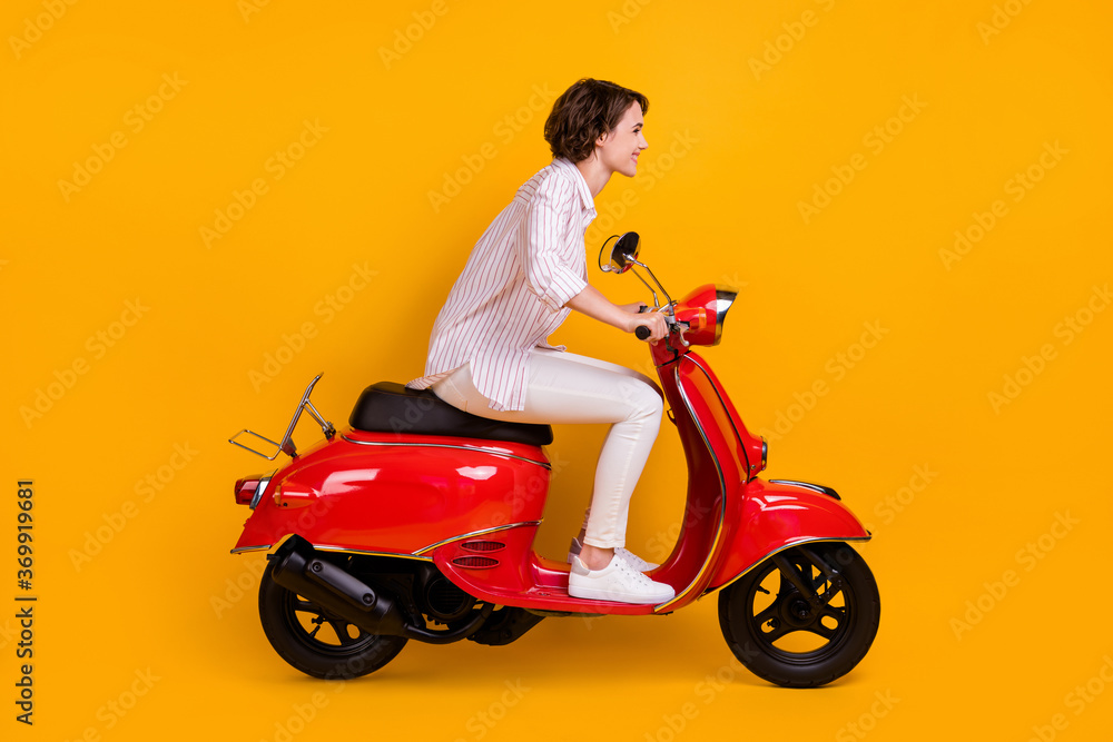 Side profile full length photo of lovely funny young girl riding scooter enjoying country road high speed lover wear white striped shirt pants isolated yellow vivid color background Side profile full length photo of lovely funny young girl riding scooter enjoying country road high speed lover wear white striped shirt pants isolated yellow vivid color background