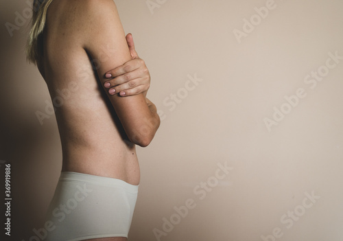 A young naked blonde woman crossed her arms on her chest on a beige background