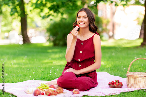 leisure and people concept - happy smiling woman eating strawberry sitting on picnic blanket at summer park © Syda Productions