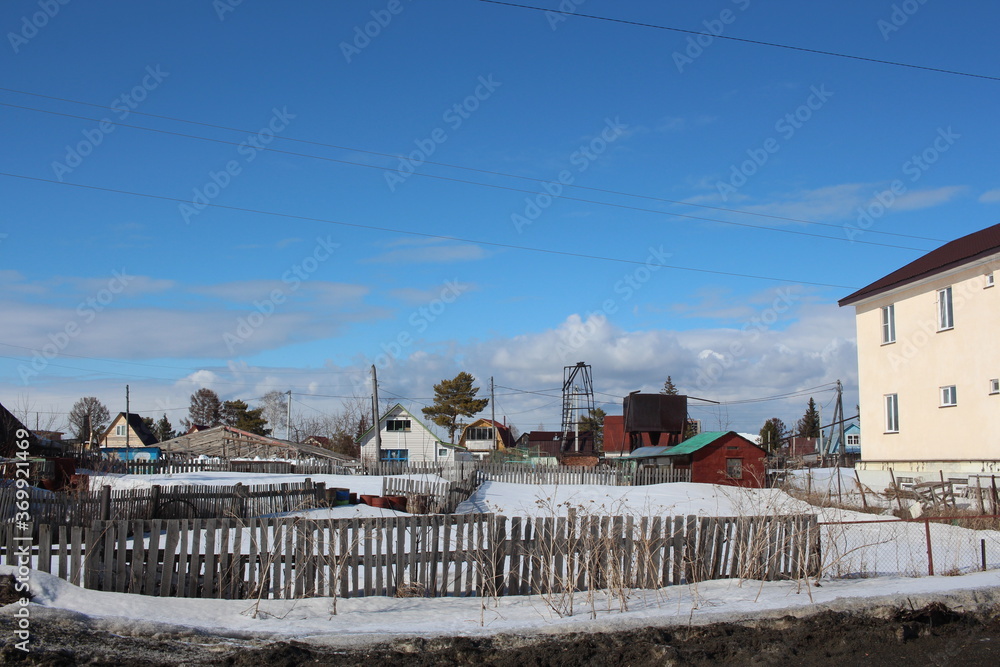 wooden houses in a Siberian village in the snow in winter with an electric pole behind a fence wooden houses in a Siberian village in the snow in winter with an electric pole behind a fence