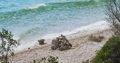 Stones stacked on a pile on a pebble beach. The waves of the beautiful turquoise sea hit the shore. A beautiful summer day on the beach Zlatni rat (Golden Horn) in Croatia.
