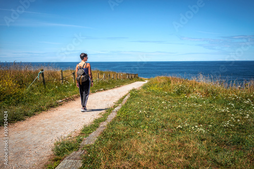 Una chica recorre un sendero que discurre junto al Mar Cantábrico.