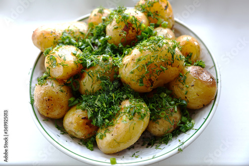 Young round fried potatoes in a kirami plate sprinkled with finely chopped dill. View from above.