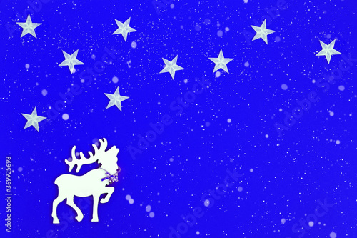 White wooden figure of deer with big horns and starry sky. Snow is falling. Concept for New Year or Merry Christmas. Christmas Holiday background. © yrabota