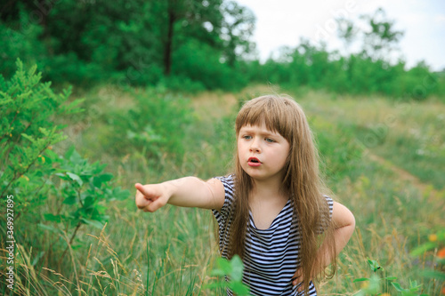 The girl shows her finger to the side on an open green background. The background is blurred.