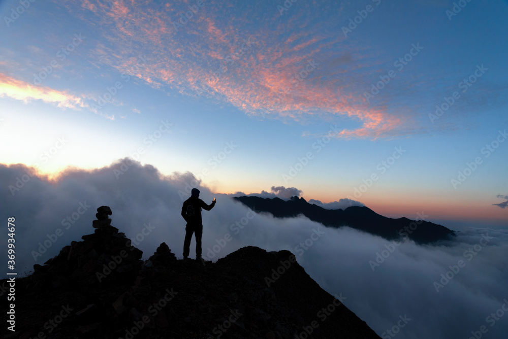 man on top of the mountain with clouds below against the background of the evening sky