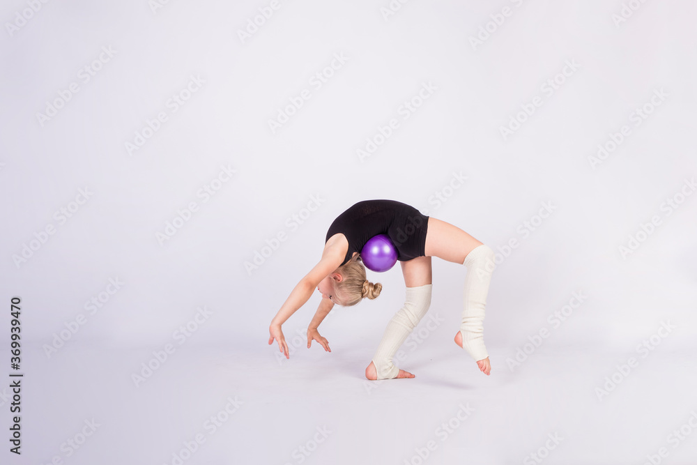 a girl gymnast in a black swimsuit does a bridge exercise with a ball on a white isolated background with space for text a girl gymnast in a black swimsuit does a bridge exercise with a ball on a white isolated background with space for text