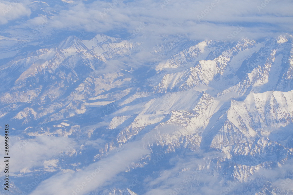 Plane window view on snowy mountain peaks in clouds