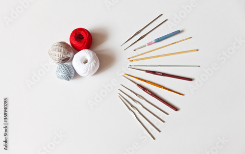 Metal, wooden and plastic crochet hooks of different sizes indicated in mm and cotton "iris" yarn for hand knitting on a white background. Needlework and hobby concept. Place for text, flat lay