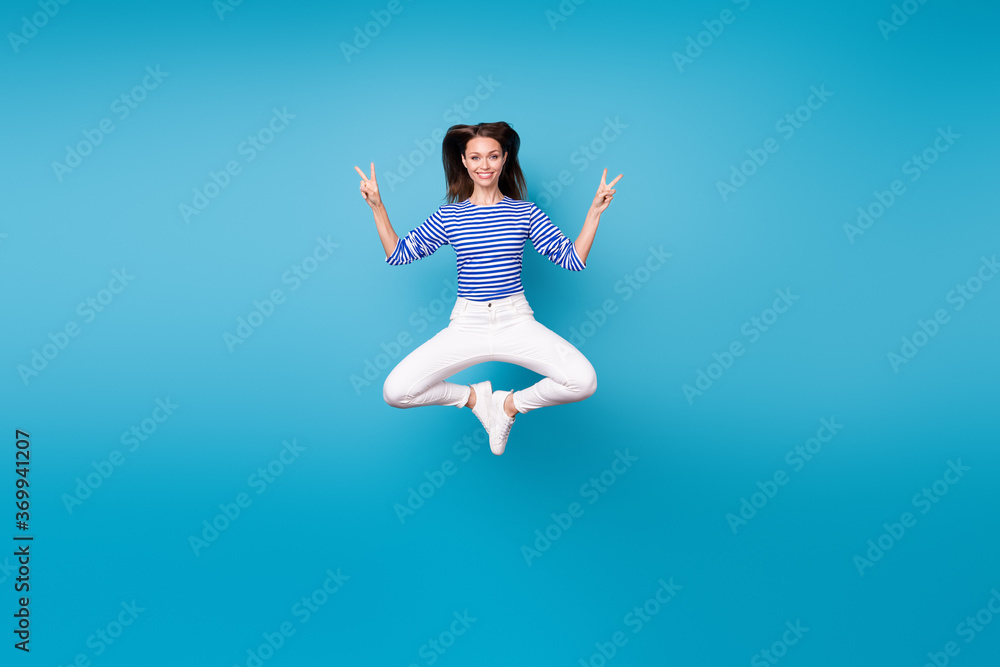 Full length body size view of her she nice attractive pretty cheerful cheery funky girl jumping having fun showing double v-sign isolated bright vivid shine vibrant blue color background