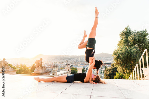 Two beautiful women doing acroyoga in the city. Harmony and relaxation with urban view