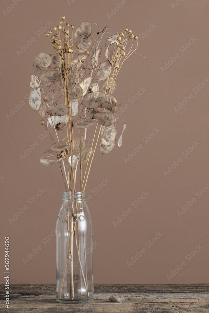 Dried flowers in a glass bottle on a wooden table on a brown background.Rustic style.
