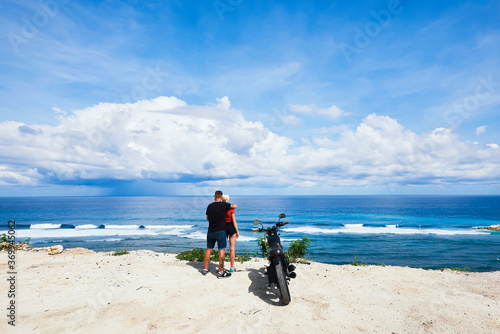 Romantic couple enjoying beautiful scenery of ocean stopping during journey traveling by motorbike, back view of lovers hugging on cost of sea fascinated with natural landscape and skyline on summer .