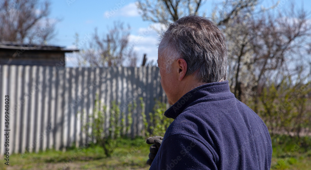 A close-up view from the back of a man of 60 years, who stands in the garden. A close-up view from the back of a man of 60 years, who stands in the garden.