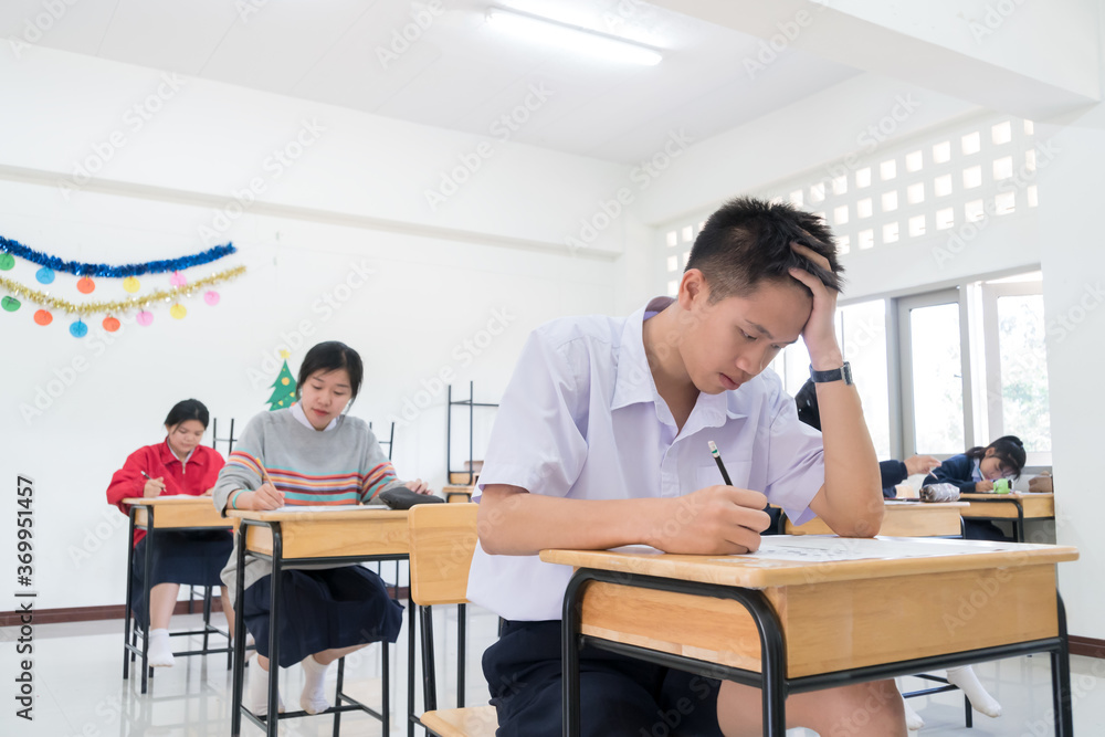 Young Asian students group serious troubled while writing exam on test paper answer sitting on taking final examination in classroom with concentration at exams room in Thailand Young Asian students group serious troubled while writing exam on test paper answer sitting on taking final examination in classroom with concentration at exams room in Thailand