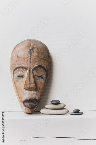 Photography African wooden mask  and zen stones on a white wall background.