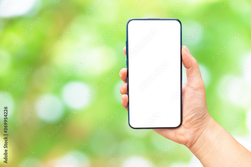 Mock up image of A hand holding a blank screen of smartphone on green bokeh blurred​ background.