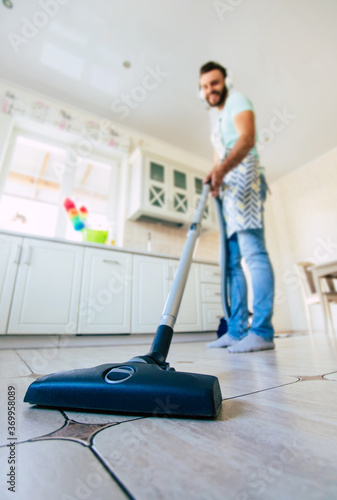 Happy handsome young beard man is cleaning the floor in the domestic kitchen and have fun.