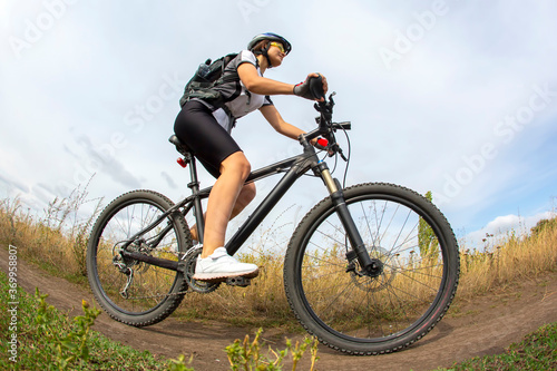 Fototapeta Naklejka Na Ścianę i Meble -  beautiful and happy girl cyclist rides a bicycle on the road in nature. Healthy lifestyle and sports. Leisure and hobbies
