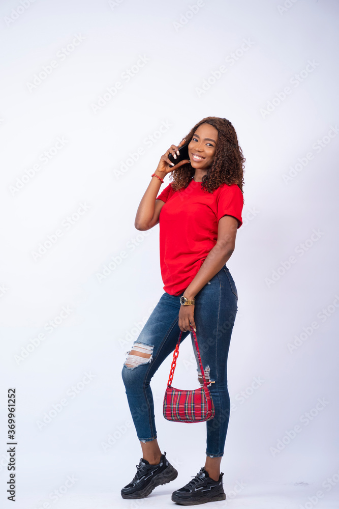 pretty african girl wearing red top and blue jeans and carrying a handbag making a phone call pretty african girl wearing red top and blue jeans and carrying a handbag making a phone call