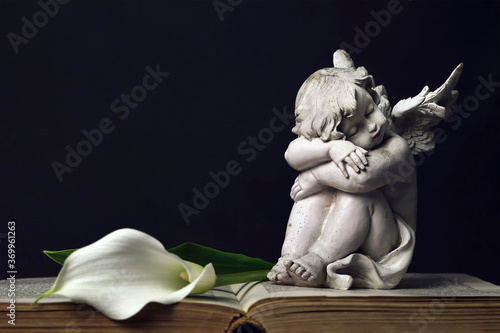 Sleeping angel and white calla lily on dark wooden background Fototapeta