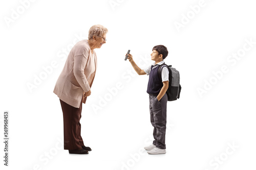 Schoolboy in a uniform standing and showing a smartphone to an older lady