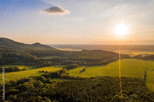 Sun shining over forested hills of Little carpathians on summer evening with a view on Zahorie area, Slovakia, Europe. Green landscape scenery from aerial perspective.