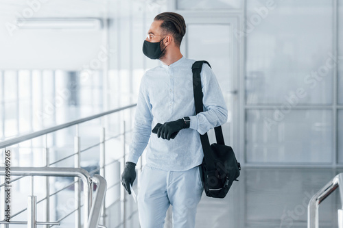 In protective mask and gloves. Young handsome man in formal clothes indoors in the office at daytime photo