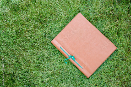 An old faded closed photo album or photo book with a red cover on the green grass on the lawn. Copy space, minimal style, the concept of storing memories.