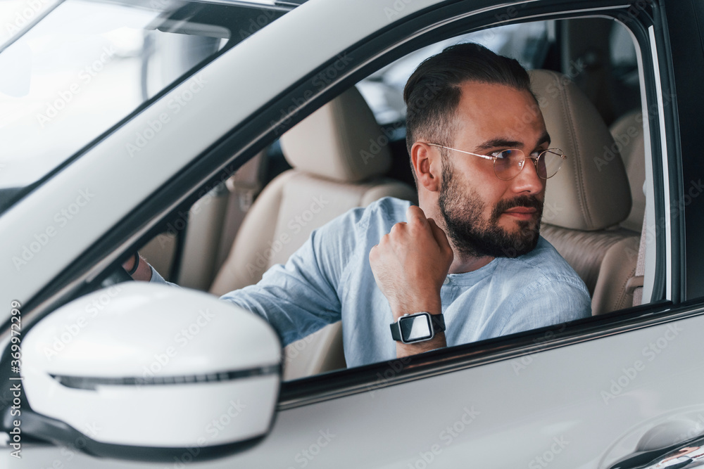 Side view of young handsome man in formal clothes that sitting in brand new automobile